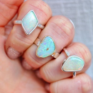 May include: Three silver rings with opal gemstones. The rings feature different shapes of opal stones, including a diamond shape, a freeform shape, and a teardrop shape.