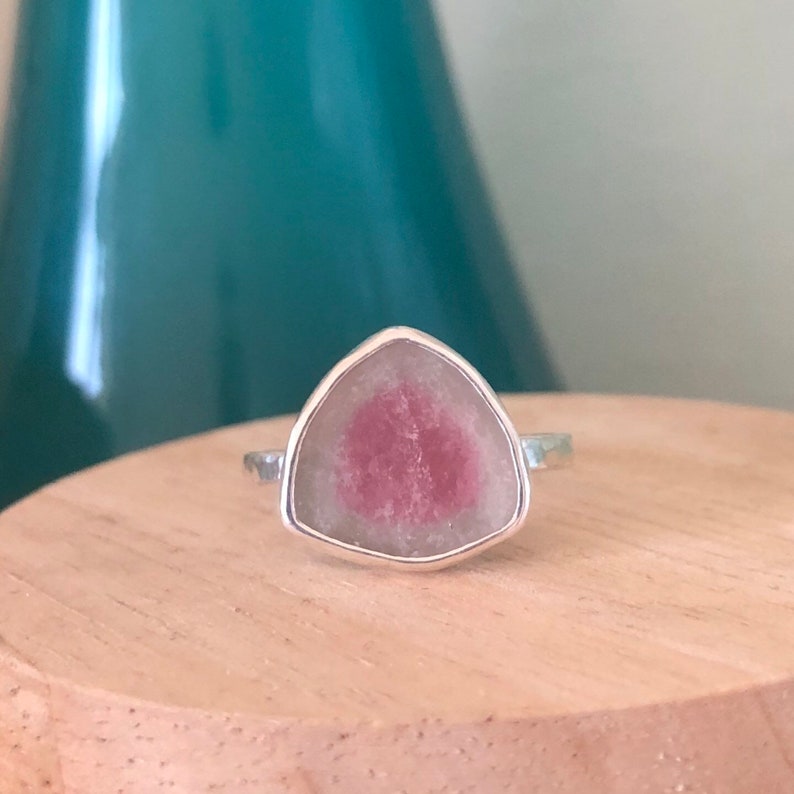 Pu&ograve; includere: Un anello d'argento con una pietra preziosa triangolare rosa e verde.
