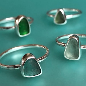 Può includere: Quattro anelli d'argento con diverse tonalità di vetro di mare verde. Ogni anello ha una texture martellata.