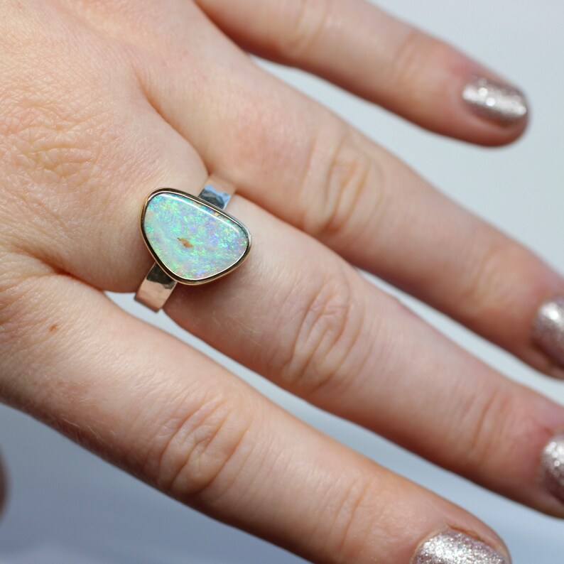 May include: A silver ring with a light green opal stone set in a gold bezel. The ring is on a finger.