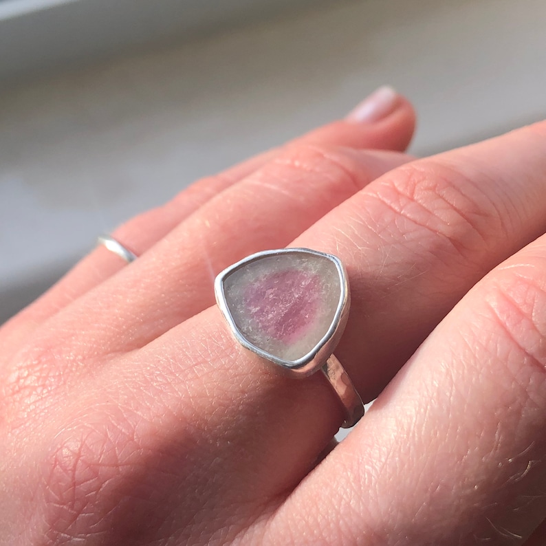 Pu&ograve; includere: Un anello d'argento con una pietra preziosa triangolare rosa e bianca.