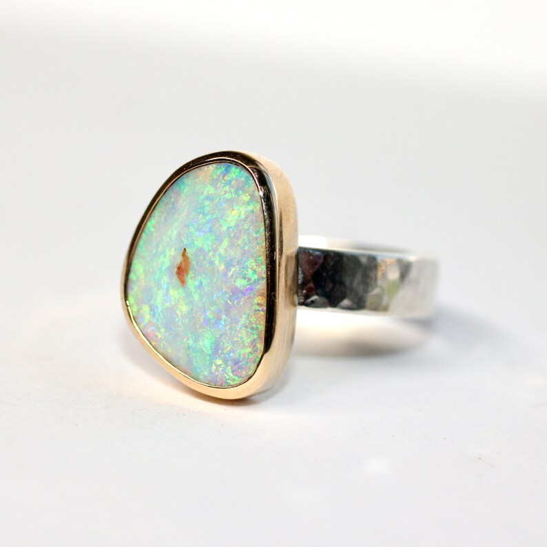 May include: A silver ring with a hammered band and a gold setting featuring a white opal gemstone.