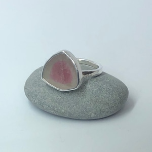 Pu&ograve; includere: Un anello d'argento con una pietra preziosa triangolare rosa e bianca incastonata al centro.