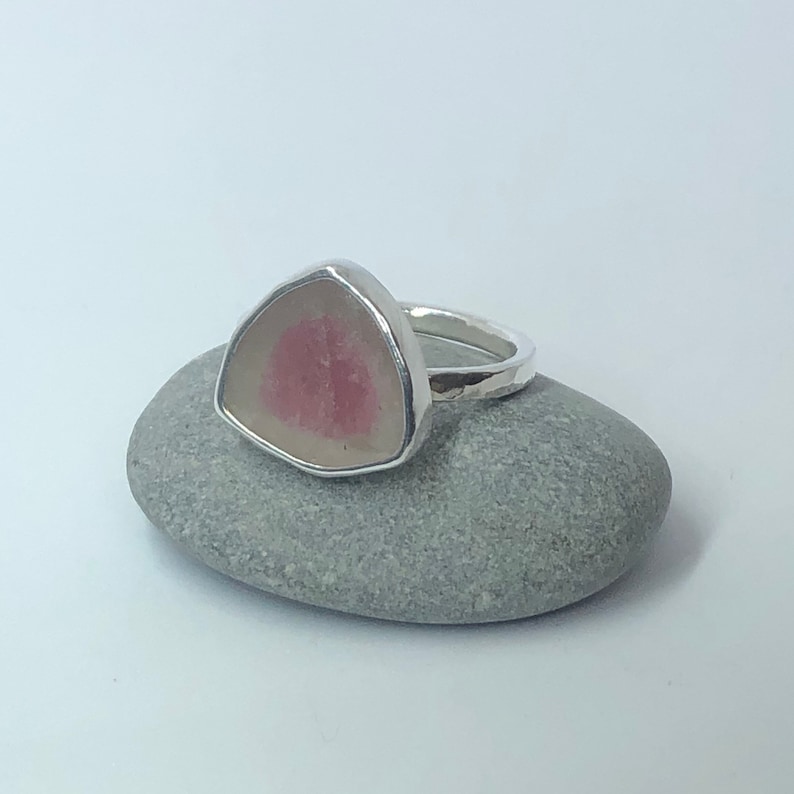 Pu&ograve; includere: Un anello d'argento con una pietra preziosa triangolare rosa e bianca incastonata al centro.
