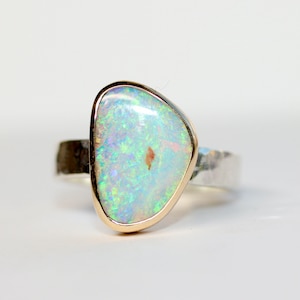May include: A silver ring with a hammered band and a gold setting featuring a white opal gemstone.