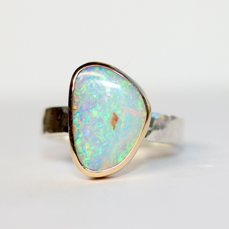 May include: A silver ring with a hammered band and a gold setting featuring a white opal gemstone.
