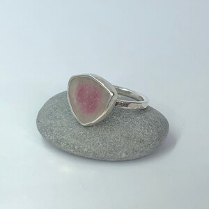 Pu&ograve; includere: Un anello d'argento con una pietra preziosa rosa e bianca incastonata in una forma triangolare.