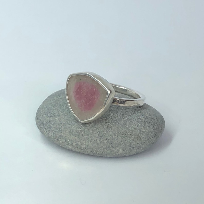 Pu&ograve; includere: Un anello d'argento con una pietra preziosa rosa e bianca incastonata in una forma triangolare.