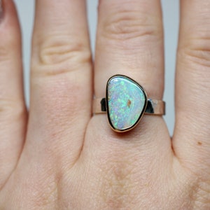 May include: A silver ring with a white opal gemstone set in a gold bezel. The opal has a green and blue iridescent sheen.