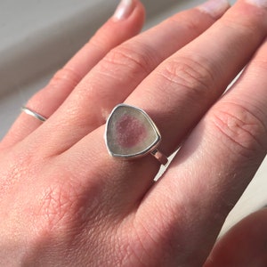 Pu&ograve; includere: Un anello d'argento con una pietra preziosa triangolare rosa e bianca incastonata al centro.