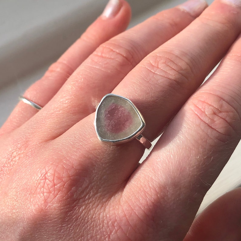 Pu&ograve; includere: Un anello d'argento con una pietra preziosa triangolare rosa e bianca incastonata al centro.