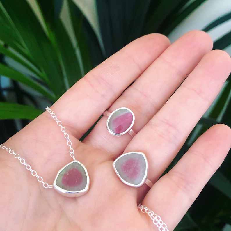 Pu&ograve; includere: Un set di tre gioielli in argento con accenti di pietre preziose rosa e verdi. I pezzi includono una collana, un anello e un anello pi&ugrave; piccolo.