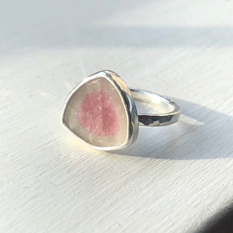 Pu&ograve; includere: Un anello d'argento con una pietra preziosa triangolare rosa e bianca incastonata al centro.