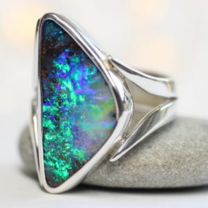 K&ouml;nnte beinhalten: Ein Silberring mit einem gro&szlig;en Opal. Der Opal zeigt ein lebendiges Farbspiel mit Gr&uuml;n-, Blau- und Lilat&ouml;nen. Das Ringdesign ist modern, mit einem schlanken, offenen Band.