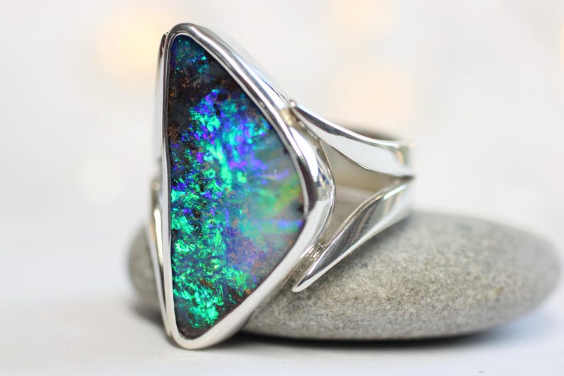 K&ouml;nnte beinhalten: Ein Silberring mit einem gro&szlig;en Opal. Der Opal zeigt ein lebendiges Farbspiel mit Gr&uuml;n-, Blau- und Lilat&ouml;nen. Das Ringdesign ist modern, mit einem schlanken, offenen Band.
