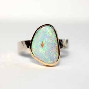 May include: A silver ring with a gold setting featuring a white opal gemstone. The opal has a pearlescent sheen and a light green hue.