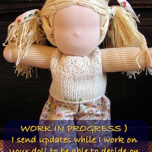May include: A doll with blonde hair in pigtails wearing a white knitted vest and a floral skirt. The doll is in progress and the caption reads "WORK IN PROGRESS) I send updates while I work on your doll to be able to decide on colors, styles, clothes later on..."