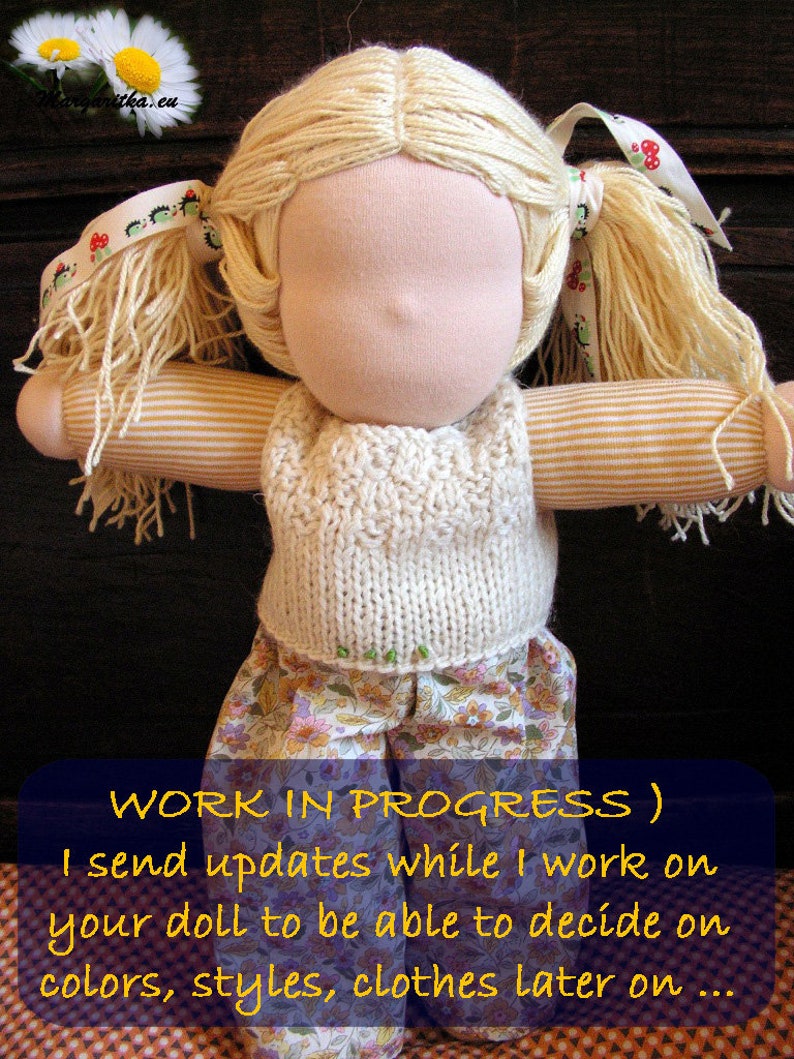 May include: A doll with blonde hair in pigtails wearing a white knitted vest and a floral skirt. The doll is in progress and the caption reads "WORK IN PROGRESS) I send updates while I work on your doll to be able to decide on colors, styles, clothes later on..."