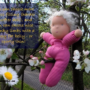 May include: A handmade doll with white yarn hair, wearing a pink and white striped outfit, sitting in a tree branch with white blossoms. The doll has a happy expression and a rosy complexion. The text "You can choose more or less filling (harder or softer doll), and you can choose nice chunky limbs with a happy fat belly - or sporty thin!" is visible in the image.