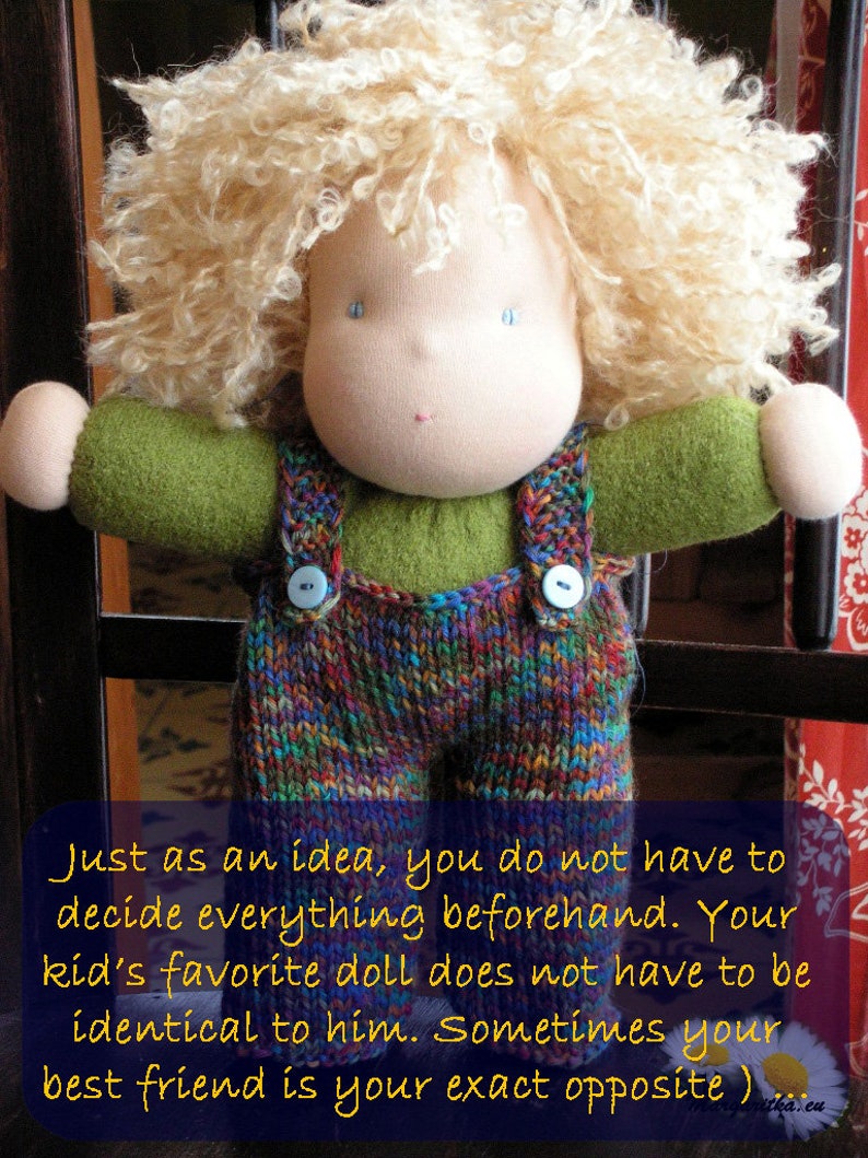 May include: A handmade doll with blonde curly hair, wearing a green shirt and colorful knitted overalls. The doll is standing in front of a wooden gate.