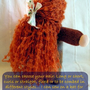 May include: A handmade doll with long, curly, orange hair. The doll has a brown body and a white bow in its hair. The doll is sitting on a white surface. You can choose your hair: Long or short, curls or straight, fixed or to be combed in different styles... I can sew on a hat for the smaller ones - with stitches that you can take away when the time is right!