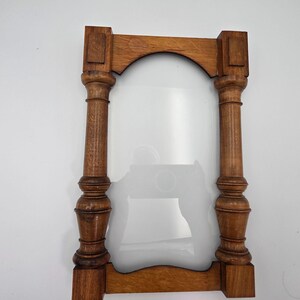 May include: A rectangular wooden picture frame featuring two vertical turned columns on the sides. The frame has a medium brown wood grain finish with a curved arch design at the top and a matching curved bottom rail connecting the two pillars.