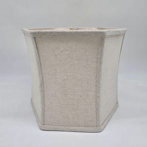 Puede incluir: Pantalla de lámpara octogonal beige con una forma ligeramente curvada. La pantalla está hecha de una tela texturizada y tiene un ribete de color claro a lo largo de los bordes superior e inferior. Diseñada para una base de lámpara.
