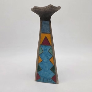 May include: A tall, ceramic vase with a flared top and a geometric design. The vase features a gray base and top, with a central column adorned with blue, yellow, and red triangles and zigzags. The vase is approximately 10 inches tall.