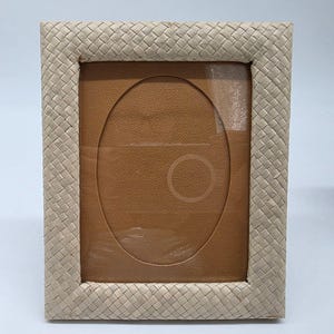 May include: Rectangular photo frame with a woven, light beige border. The frame has an oval opening and a brown backing. The woven border adds a textured, natural element to the frame, suitable for displaying photographs or artwork.