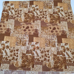 May include: A patchwork textile with a repeating pattern of squares in shades of brown, beige, and cream. The squares feature floral and leaf motifs, creating a warm, autumnal aesthetic. The fabric appears to be a quilt or similar decorative textile, possibly for a bedspread.
