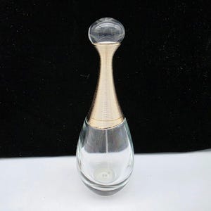 May include: A clear glass perfume bottle with a gold-colored neck and a clear, spherical top. The bottle has a teardrop shape and is empty. The gold neck has a ribbed design.