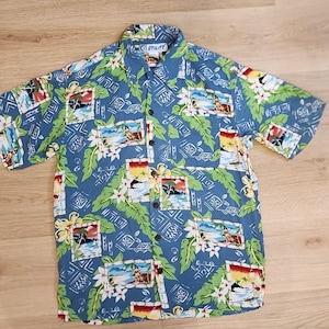 May include: Blue short-sleeve button-down shirt with a tropical print. The shirt features a pattern of beach scenes, flowers, and geometric shapes. The collar has the word "UTILITY" printed on it.