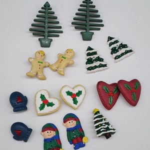 Puede incluir: Una colección de botones con temática navideña en varias formas y colores. Incluye árboles de Navidad verdes, hombres de jengibre, corazones, mitones y figuras de elfos. Los botones son de plástico y tienen un acabado brillante.