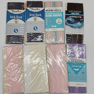 Könnte beinhalten: Eine Sammlung von Vintage-Nähutensilien, darunter Trimtex Rick Rack in Marineblau und Schwarz, Wrights Flexi-Lace Nahtband in Rosa und Lila sowie Wrights Soft and Easy Hemtape in Braun. Die Verpackungen weisen Text und Preise auf.