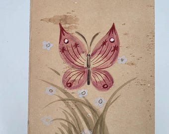 Può includere: Una superficie rettangolare color marrone chiaro con un'illustrazione dipinta a mano di una farfalla rosa con dettagli delle ali rosso scuro. Sotto la farfalla, fili d'erba verdi e piccoli fiori bianchi sono dipinti sullo sfondo testurizzato.