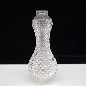Puede incluir: Jarrón de cristal transparente con exterior con diseño de diamantes. El jarrón tiene una base bulbosa, una sección media delgada y texturizada y una parte superior ensanchada. El jarrón mide aproximadamente 18 cm de alto.