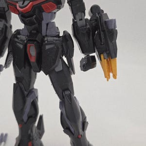 Peut inclure: Gros plan sur une figurine robotique noire et grise avec des d&eacute;tails rouges et jaunes. Le bras de la figurine est tendu, r&eacute;v&eacute;lant des composants m&eacute;caniques complexes et des angles vifs. Le design sugg&egrave;re un th&egrave;me futuriste ou de science-fiction.