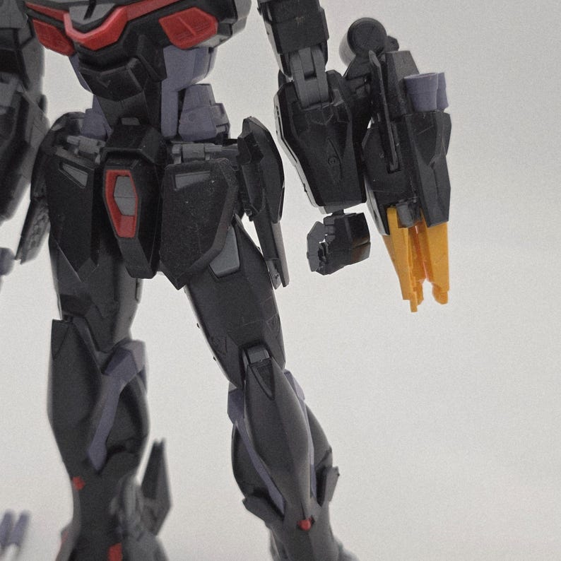 Peut inclure: Gros plan sur une figurine robotique noire et grise avec des d&eacute;tails rouges et jaunes. Le bras de la figurine est tendu, r&eacute;v&eacute;lant des composants m&eacute;caniques complexes et des angles vifs. Le design sugg&egrave;re un th&egrave;me futuriste ou de science-fiction.