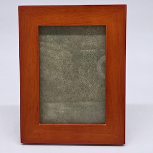 May include: A rectangular wooden picture frame with a warm, reddish-brown finish. The frame has a simple, classic design and a glass or clear plastic insert to protect the photo. The frame is designed to hold a standard-sized photograph.