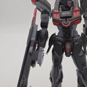 Peut inclure: Maquette de robot partiellement assembl&eacute;e, avec des &eacute;l&eacute;ments noirs, gris et rouges. Le kit comprend une grande arme lat&eacute;rale. Le mod&egrave;le pr&eacute;sente des d&eacute;tails m&eacute;caniques complexes, typiques des maquettes, avec une attention particuli&egrave;re &agrave; la pr&eacute;cision.