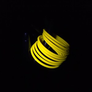 May include: A coiled arrangement of bright yellow, flexible tubing against a black background. The tubing appears to be made of a soft, pliable material, and is tightly wound into a spiral shape. The overall effect is a striking contrast of colour and form.