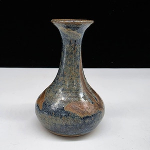 May include: A handcrafted ceramic vase with a bulbous base and a slender neck. The vase features a blend of blue, brown, and tan hues, creating a textured, earthy appearance. The vase is approximately 7 inches tall, perfect for displaying flowers or as a decorative piece.