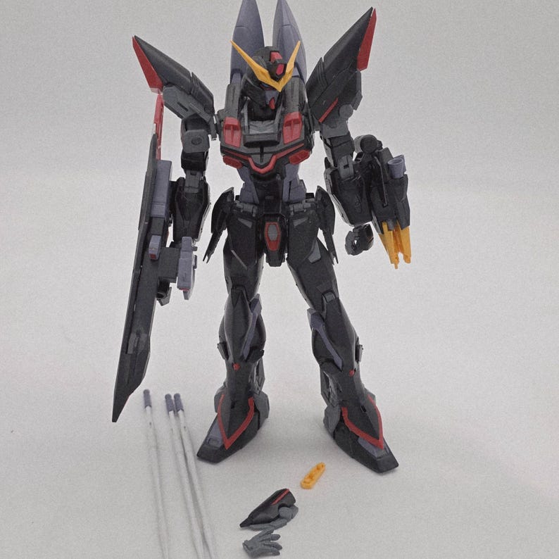 Peut inclure: Maquette d&eacute;taill&eacute;e d'un robot m&eacute;cha noir et rouge avec des accents gris et jaunes. Le robot a une grande arme sur le c&ocirc;t&eacute; gauche et plusieurs pi&egrave;ces d&eacute;tach&eacute;es. Le mod&egrave;le est debout sur une surface blanche.