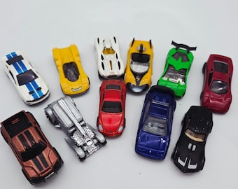 May include: A collection of toy cars in various colors, including white with blue stripes, yellow, white, yellow, green, red, brown, silver, red, blue, and black. The toy cars are arranged on a white surface.