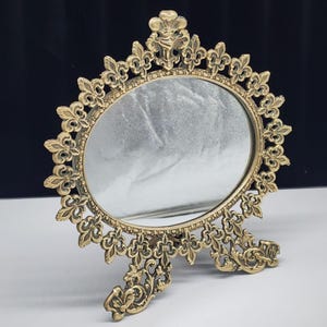 Espejo de mesa ovalado ornamentado de latón antiguo con diseño de flor de lis y soporte de caballete
