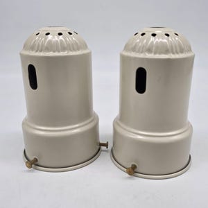 Peut inclure: Deux douilles de lampe beiges de forme cylindrique. Chaque douille a un dessus décoratif avec de petits trous, une ouverture latérale et une vis de couleur laiton. Les douilles sont présentées sur fond blanc.