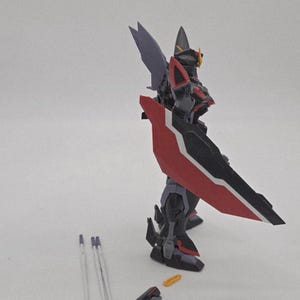 Peut inclure: Mod&egrave;le d&eacute;taill&eacute; de robot aux couleurs rouge, noir et gris. Le robot est &eacute;quip&eacute; d'un grand bouclier et de structures en forme d'ailes. Des pi&egrave;ces suppl&eacute;mentaires sont visibles &agrave; proximit&eacute;.