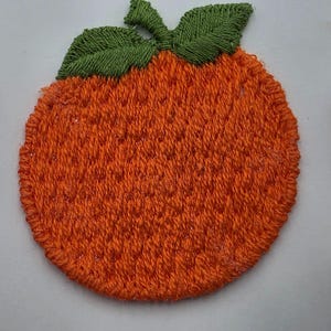 May include: A circular embroidered patch featuring a vibrant orange fruit design. The patch is stitched with bright orange thread for the body of the fruit and deep green thread for the two leaves at the top, creating a textured surface.