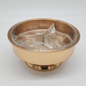 Puede incluir: Un plato para servir vintage con un inserto de vidrio transparente dividido en tres secciones. El plato tiene una base y un borde de metal dorado, con una base de pedestal. El inserto de vidrio tiene un patrón de estrella.