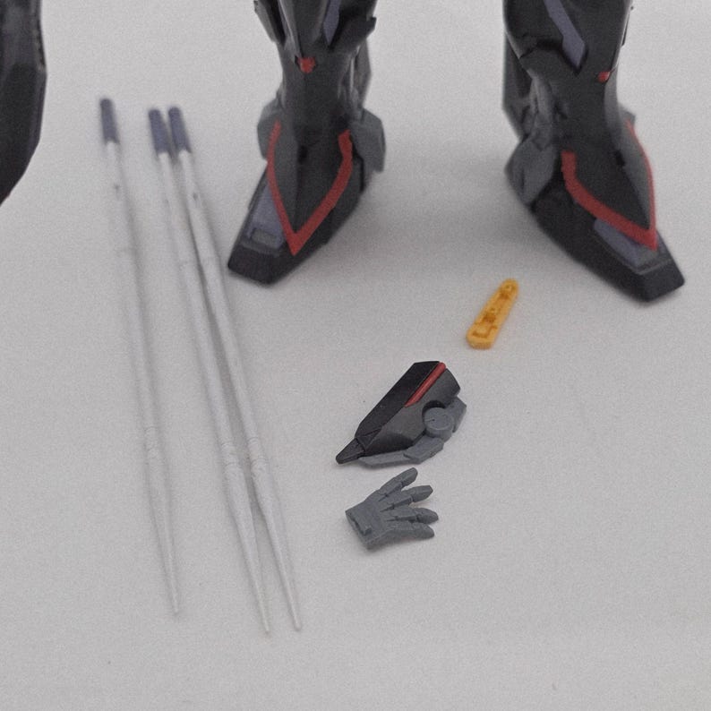 Peut inclure: Gros plan d'une figurine articul&eacute;e d&eacute;taill&eacute;e avec divers accessoires. Les jambes de la figurine sont noires avec des d&eacute;tails rouges. Les accessoires comprennent des tiges blanches, une main grise et d'autres petites pi&egrave;ces.